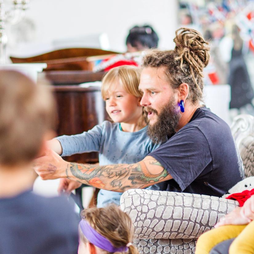 Bilde av en barnehageansatt som sitter i en stol med et barn på fanget. Foto: Krafttak for sang