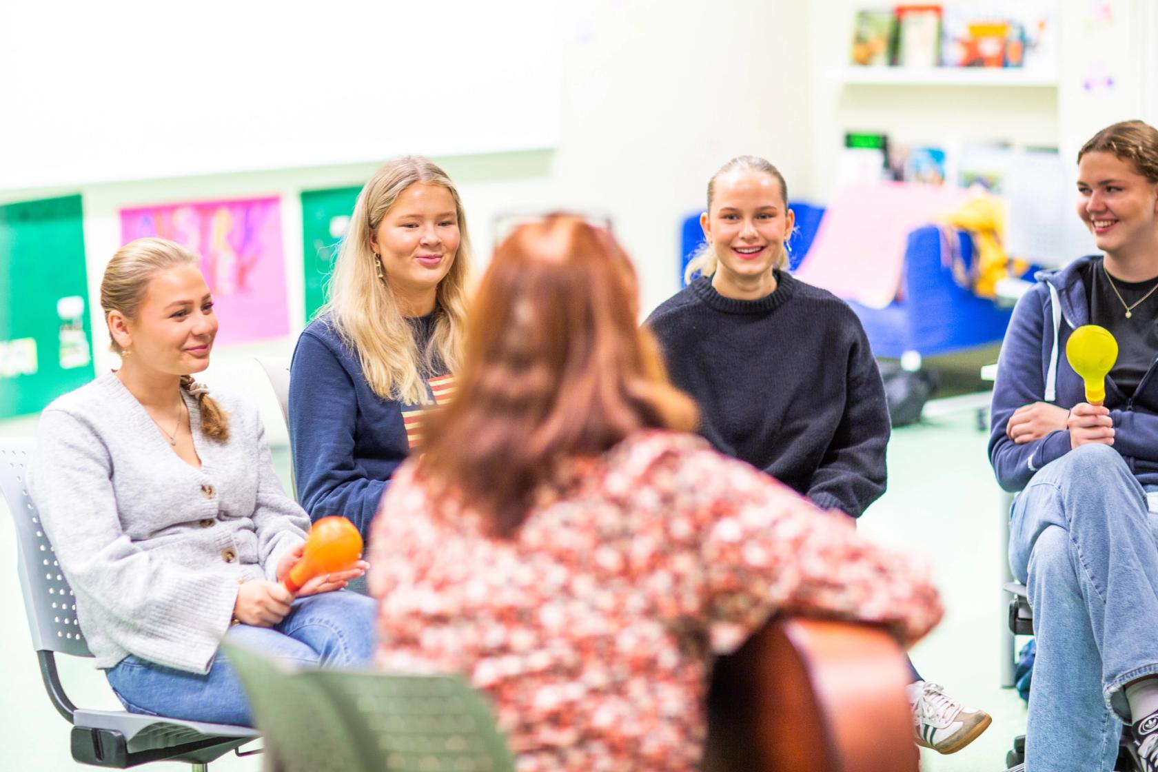 En lærer spiller gitar sammen med fire elever. Foto. Krafttak for sang