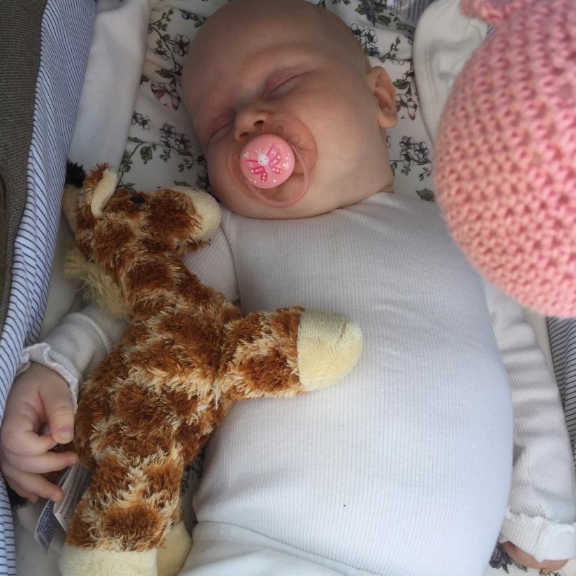 Bilde av et lite barn som sover søtt i vognen sin med bamser rundt seg