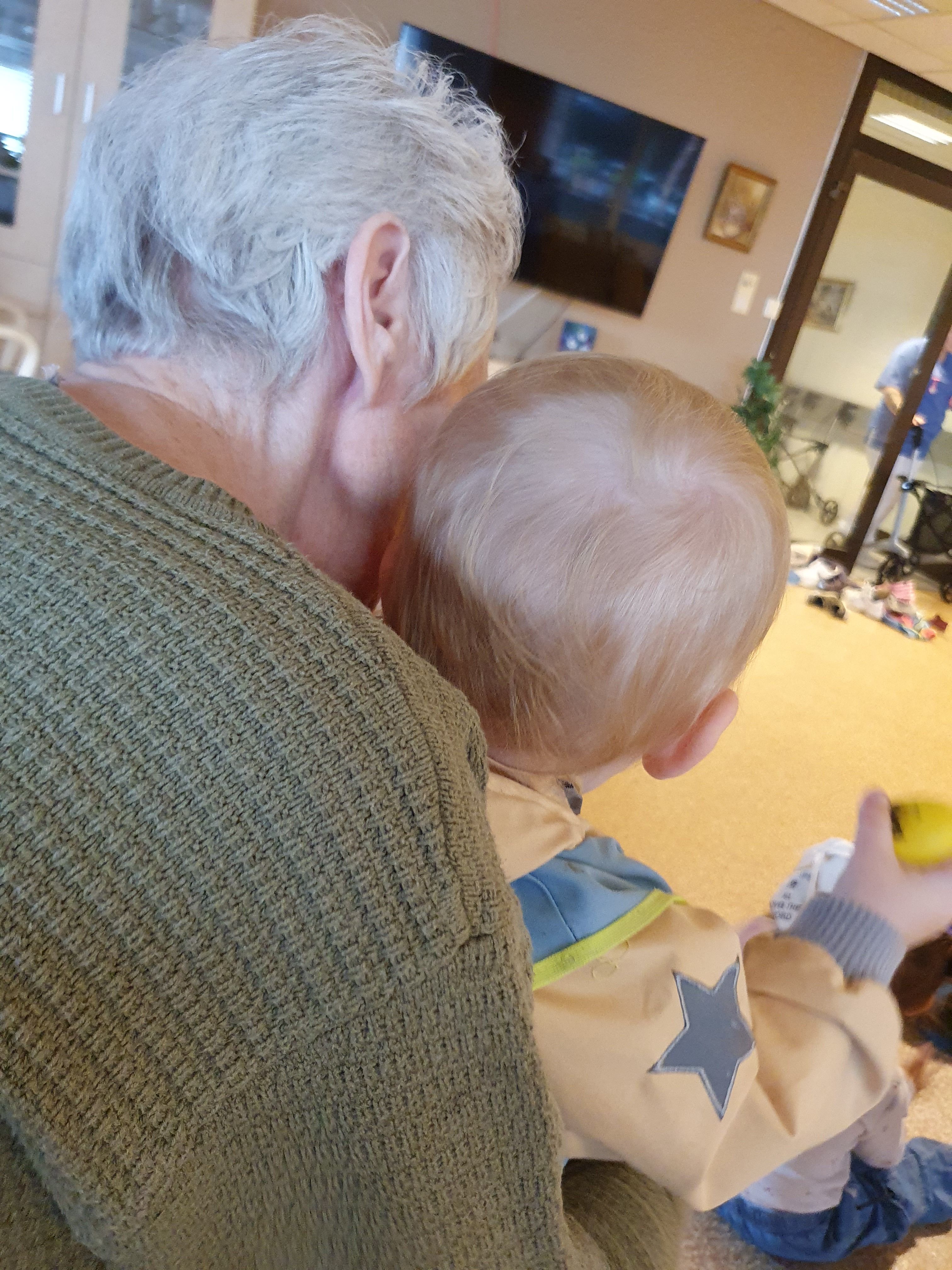 Bilde av et lite barn som sitter på fanget til en gammel dame