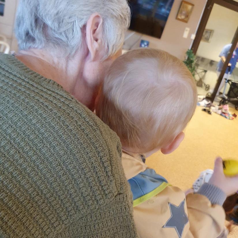 Bilde av et lite barn som sitter på fanget til en gammel dame