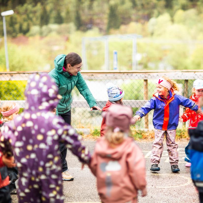 Bilde av barnehagebarn og en ansatt som har ringlek ute.