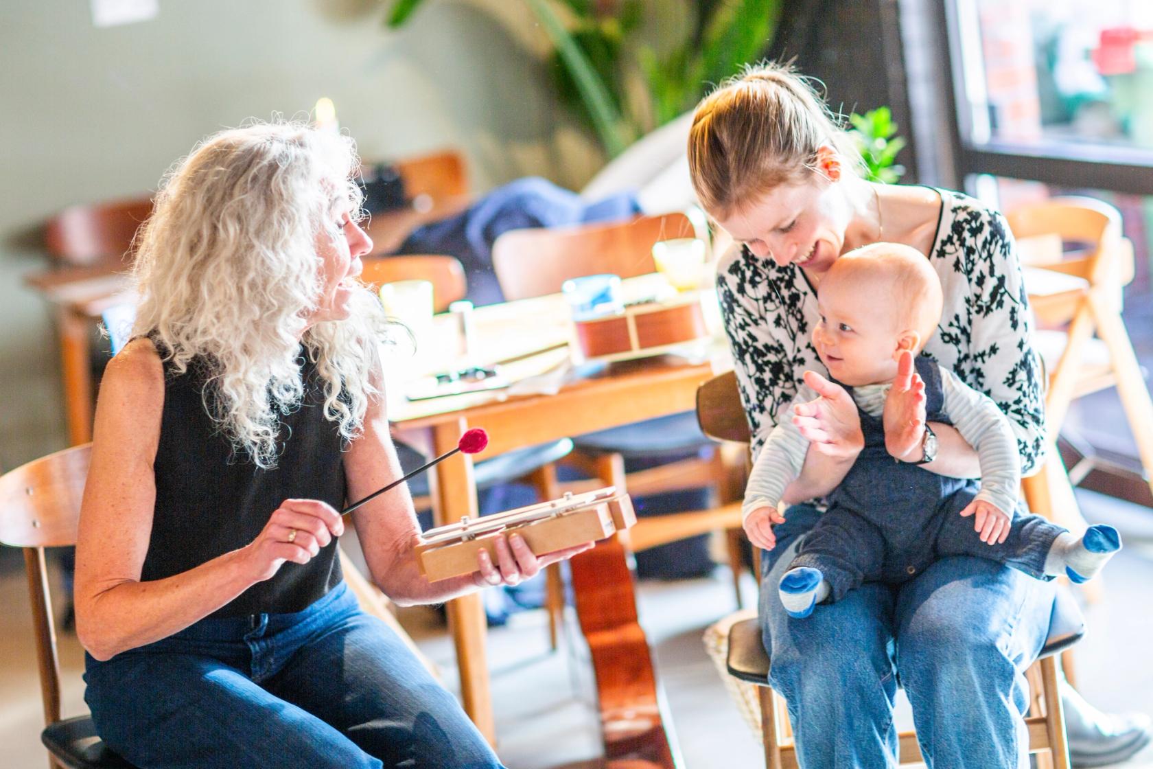 Bilde av en musikkpedagog som synger og spiller for en mor med baby. Foto: Krafttak for sang