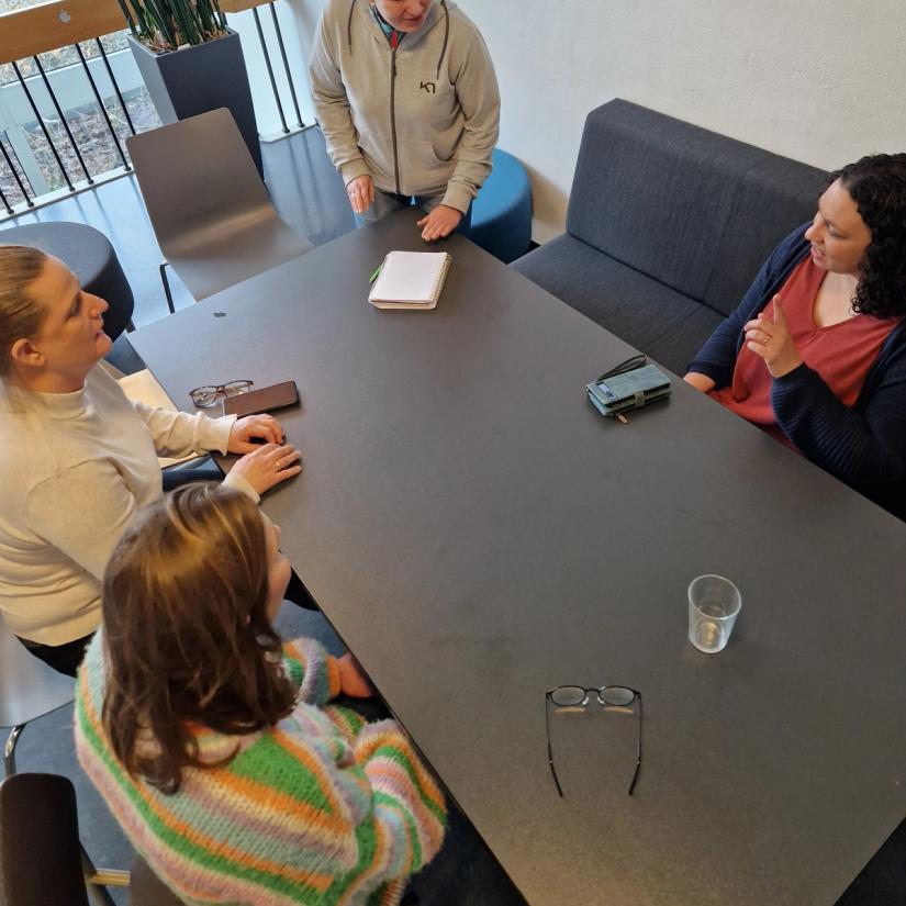 Vi ser fem damer som sitter rundt et bord og gjør gruppearbeid på kurs.
