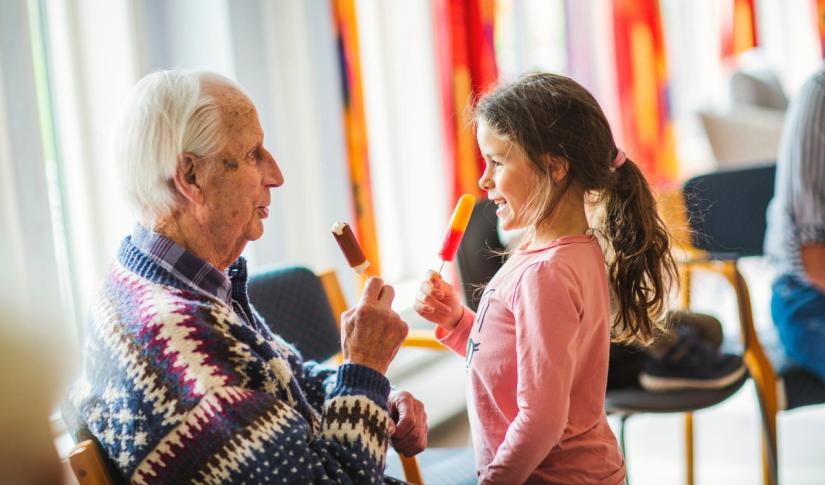En jente fra en barnehage og en beboer spiser is. Foto: Krafttak for sang