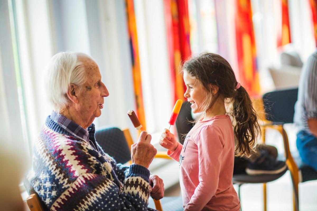 Bilde av en gammel mann og en liten jente som ser på hverandre og spiser is