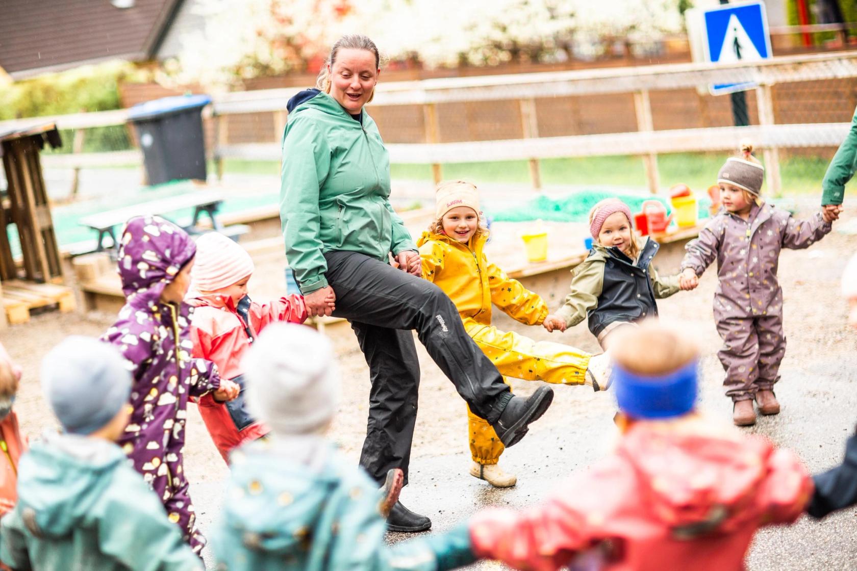 En ansatt danser i ring med barna i en barnehage, ute. Foto: Krafttak for sang