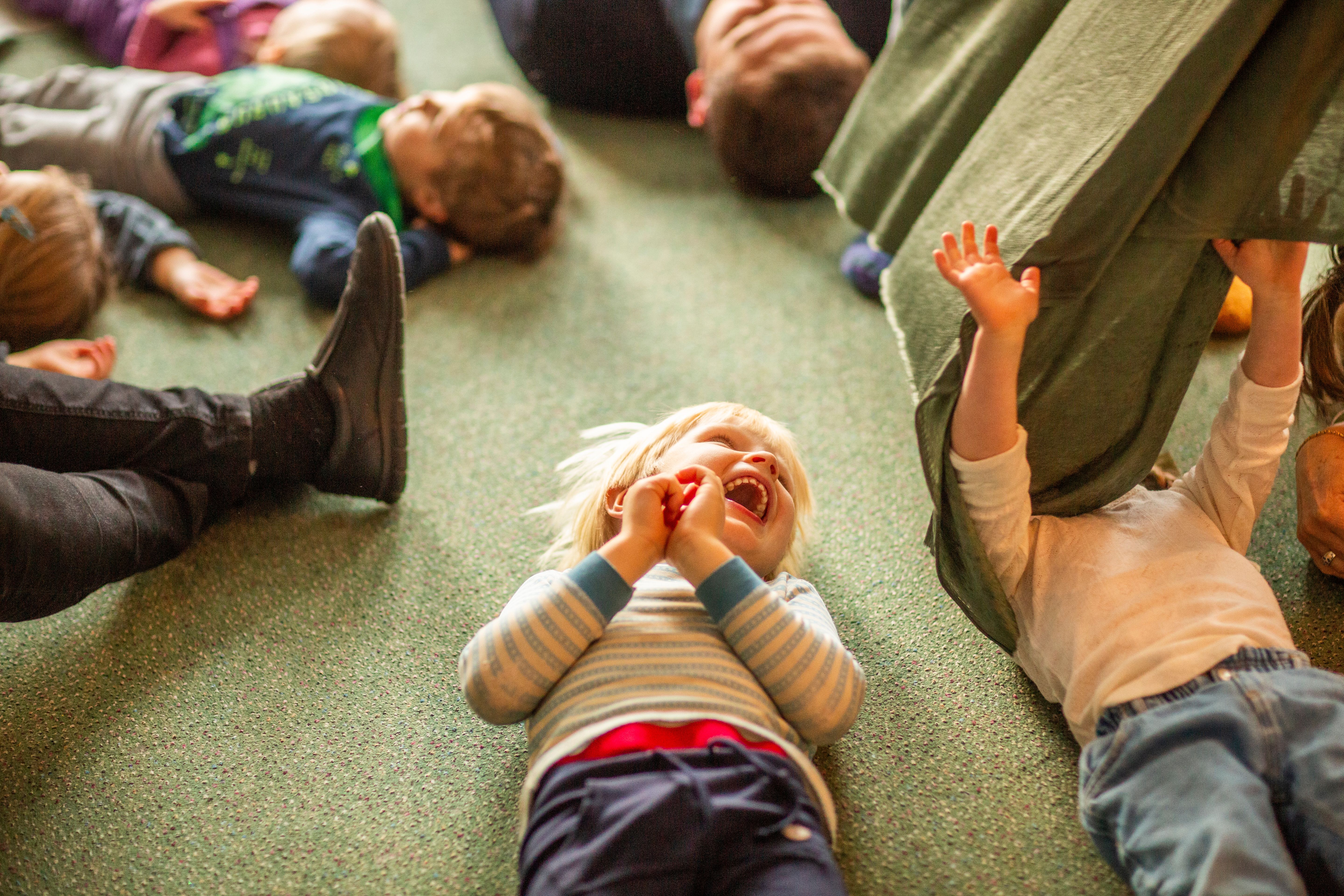Bildet viser lekende barn som ligger i ring på gulvet. 