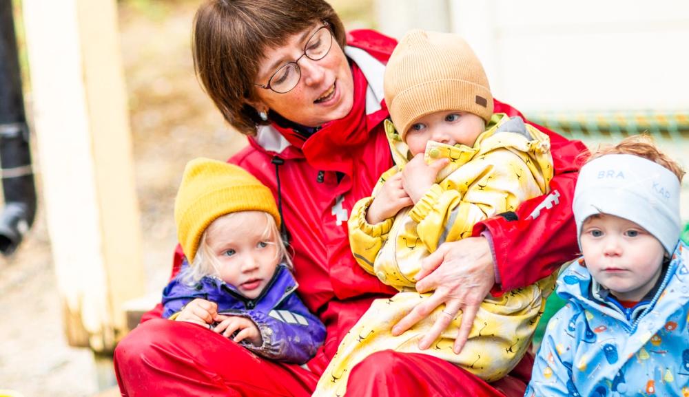 En barnehageansatt sitter med to barn på fanget og synger. Foto: Krafttak for sang