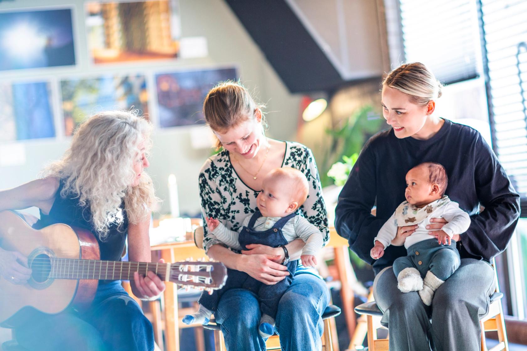 Bilde av to mødre med sine babyer sammen med musikkpedagog med gitar. Foto: Krafttak for sang