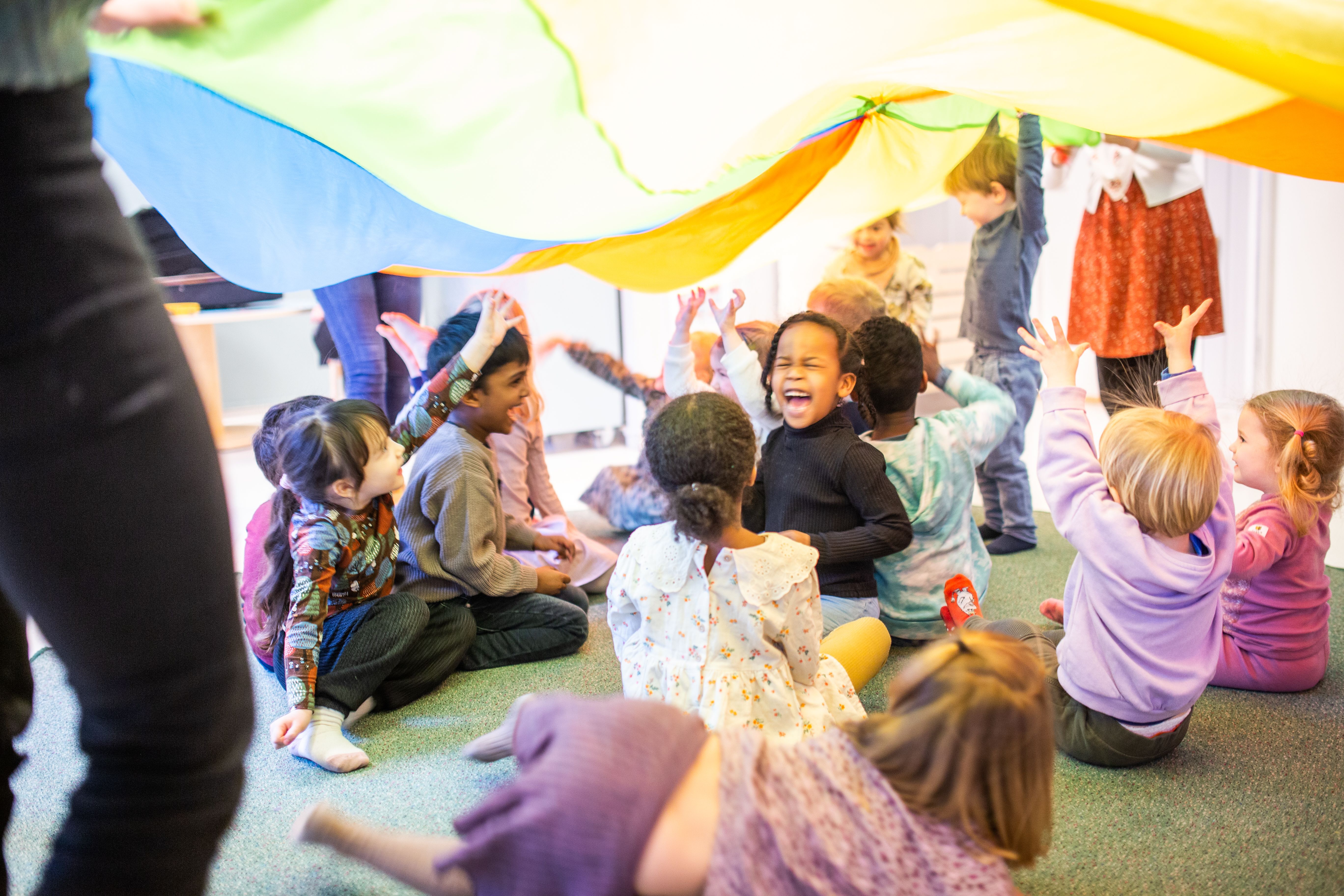 Bilde av en gruppe barn som sitter under en fallskjerm, smiler og ler