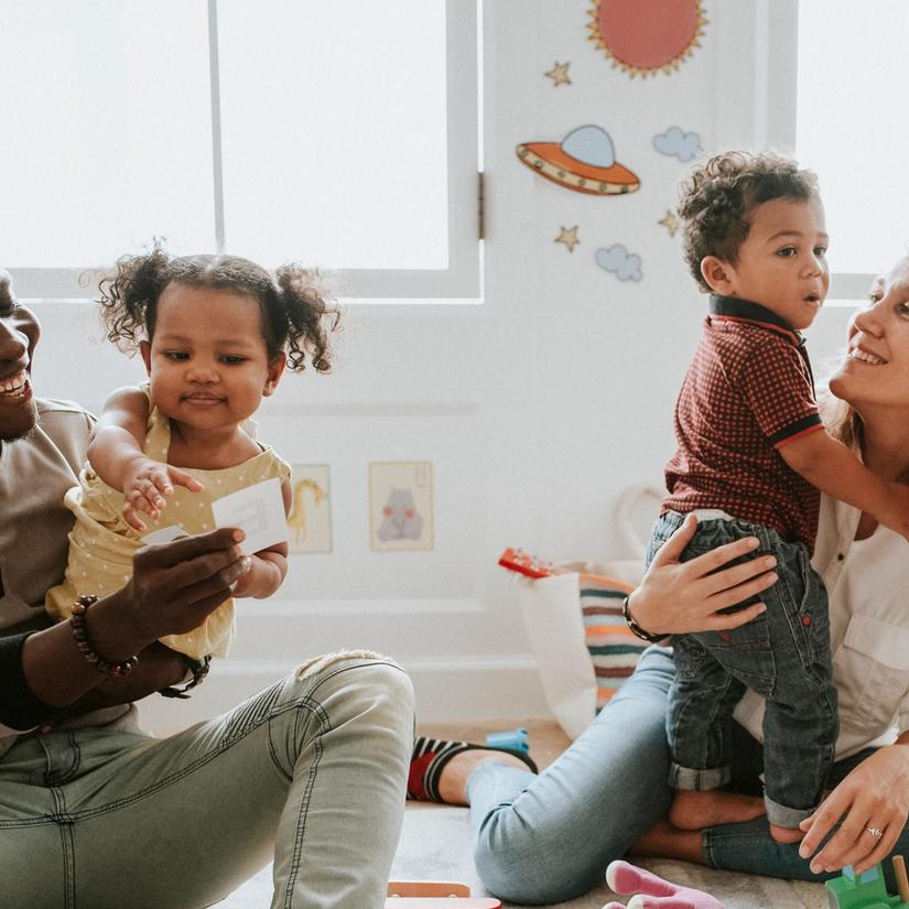 Bilde av to foreldre med sine barn som sitter på gulvet i en barnehage og leker sammen