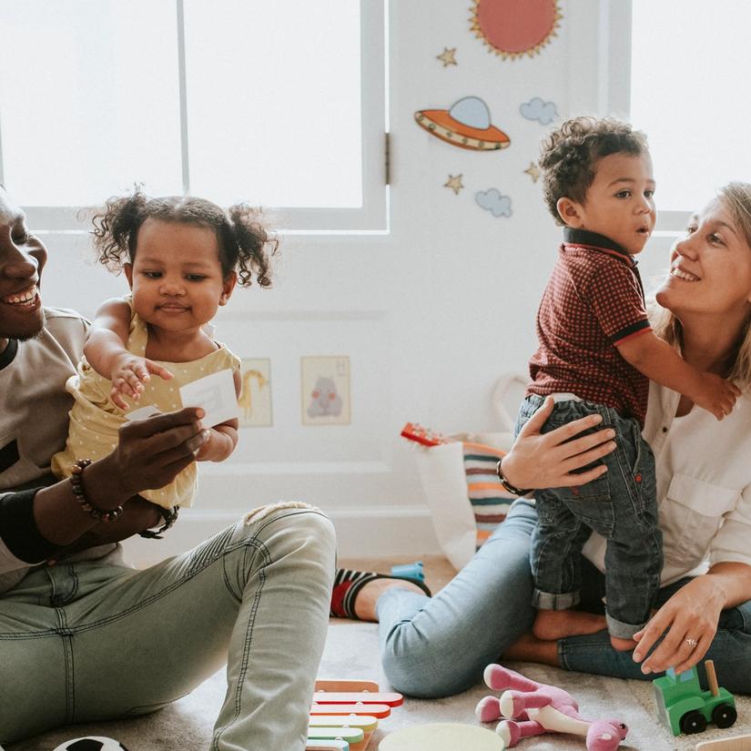 Bilde av to foreldre som leker med sine barn på gulvet i en barnehage
