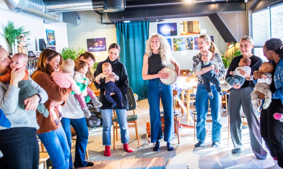 En gruppe mødre og deres babyer danser sammen med en musikkpedagog som spiller tromme