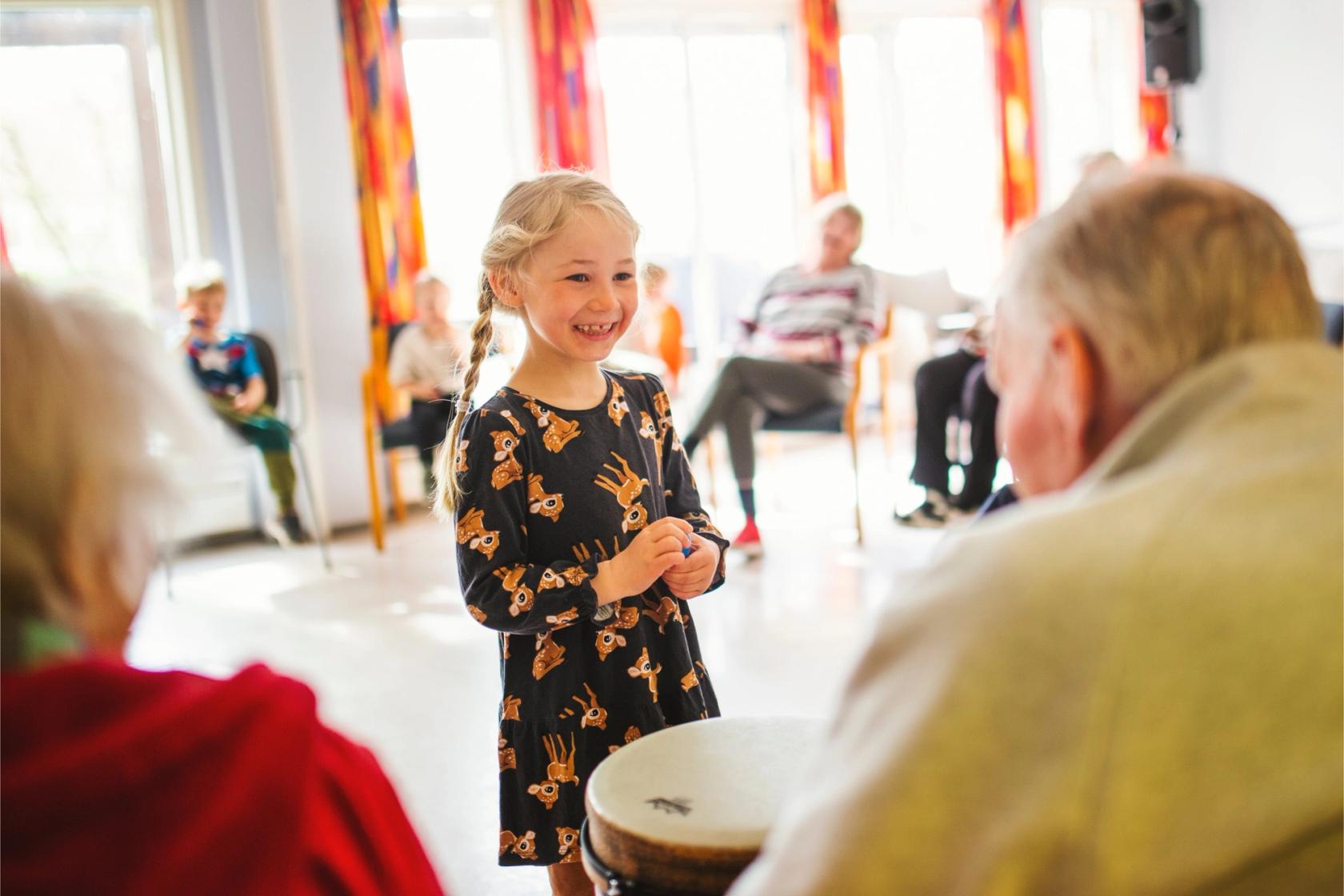 En jente står foran noen beboere på en eldreinstitusjon i sangstund. Foto: Krafftak for sang