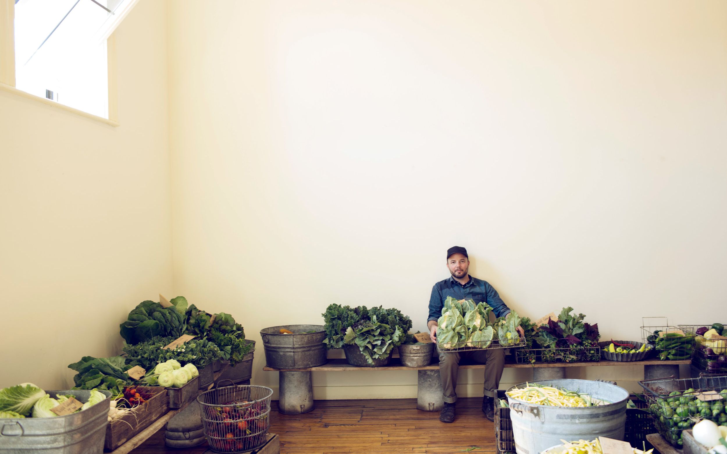 Joshua McFadden sitting in a large sunny room surrounded by baskets of fresh produce