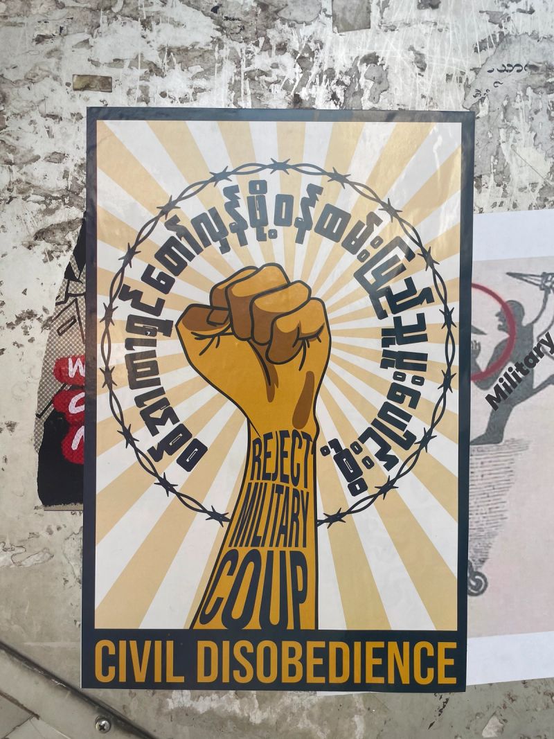 A Myanmar resistance poster featuring a raised golden fist encircled by barbed wire with the text "Reject Military Coup" and "Civil Disobedience" in English and Burmese.