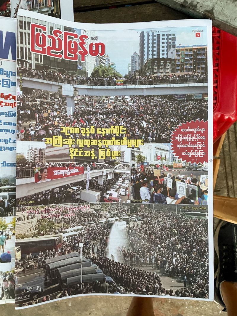 Front page of the Burmese-language newspaper Pyi Myanmar from 2021, featuring photographs of massive street protests in Yangon following the military coup. The headline reports 300,000 people taking to the streets, with images showing crowds on overpasses and water cannons deployed against demonstrators.