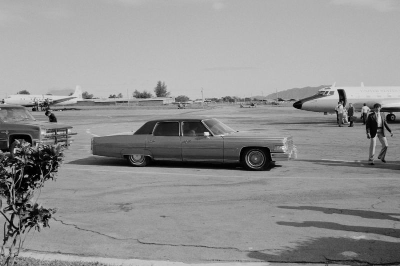 An armored Cadillac car belonging to the United States Embassy pulls up to an arriving U.S. government jet plane in Ilopango, El Salvador, November 1, 1982. © Nickelsberg