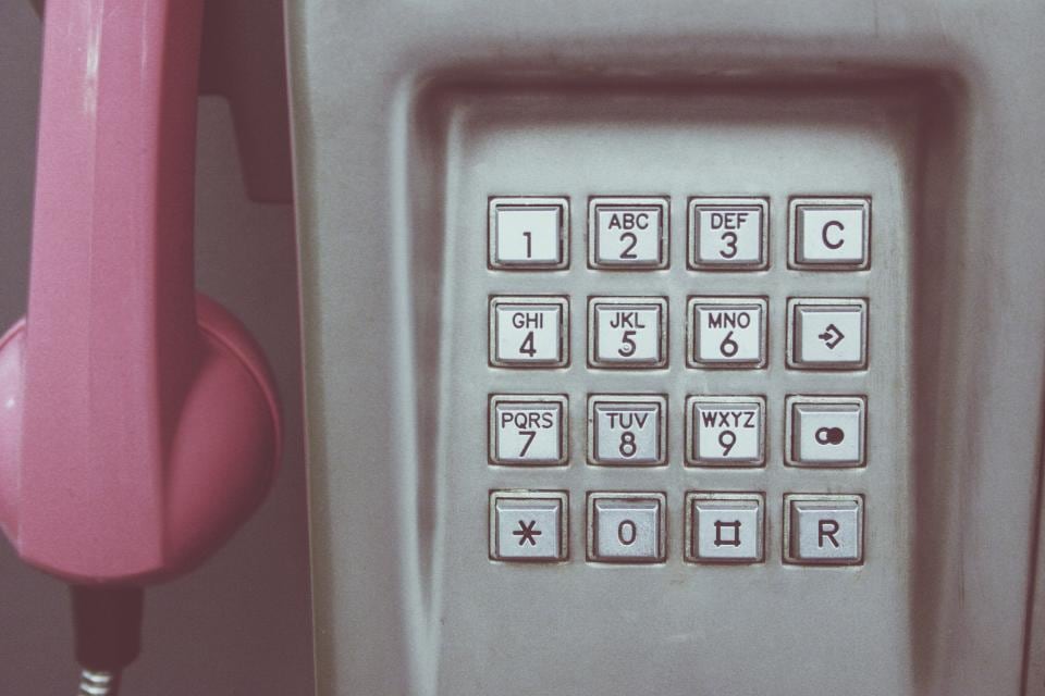 Un combiné rose décroché devant le clavier d’une cabine téléphonique
