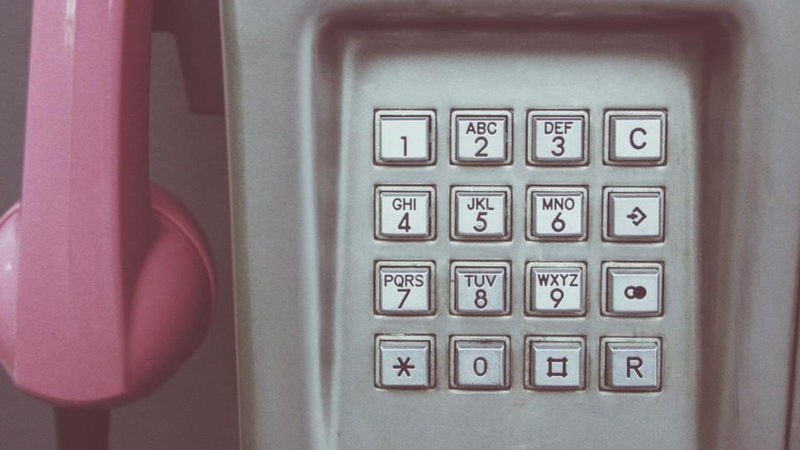 Un combiné rose décroché devant le clavier d’une cabine téléphonique