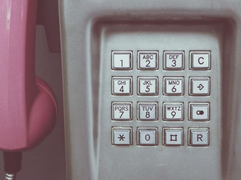 Un combiné rose décroché devant le clavier d’une cabine téléphonique