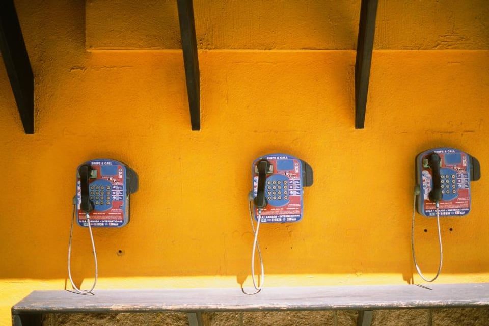 Trois téléphones publics accrochés à un mur jaune