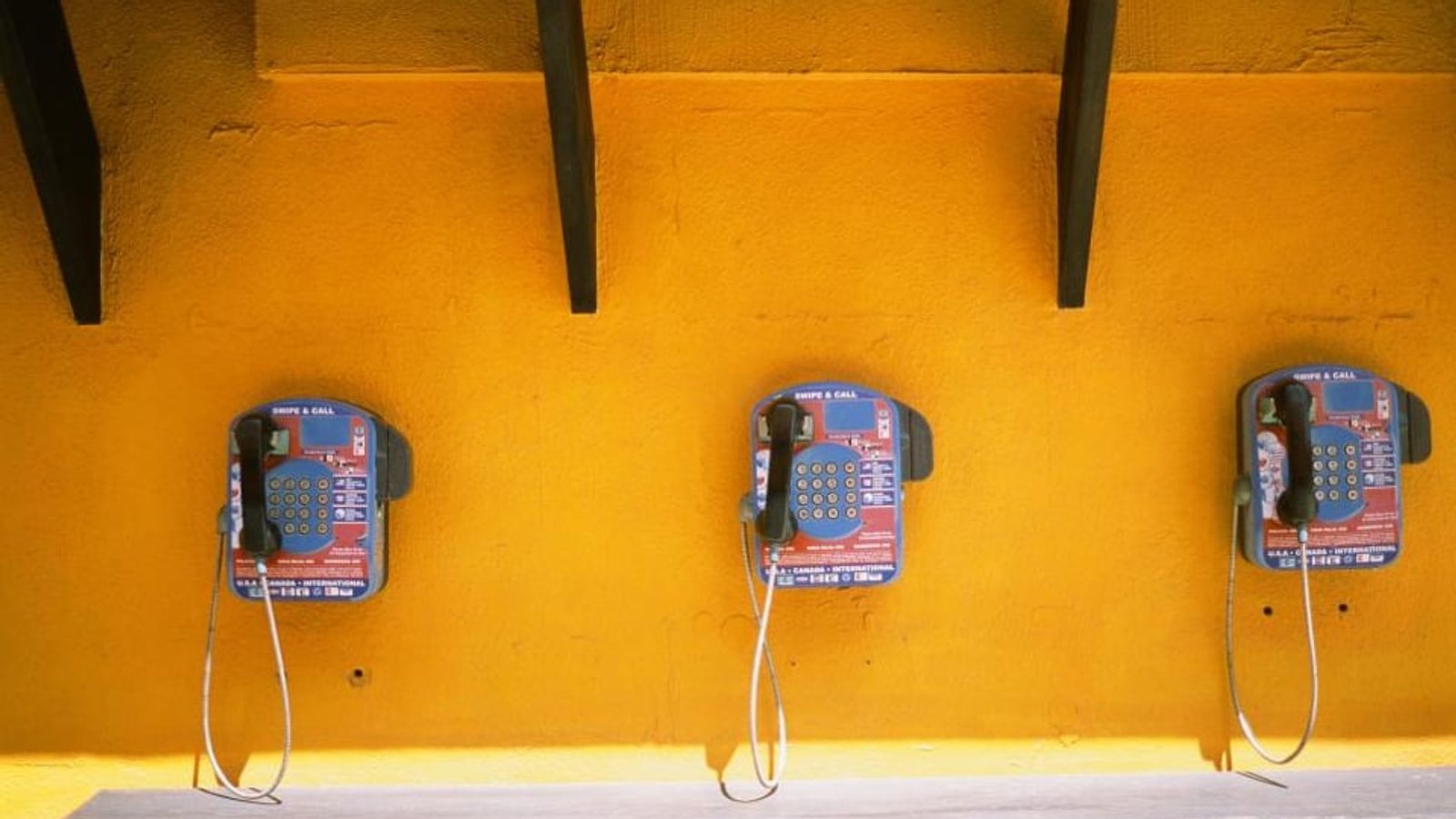 Trois téléphones publics accrochés à un mur jaune