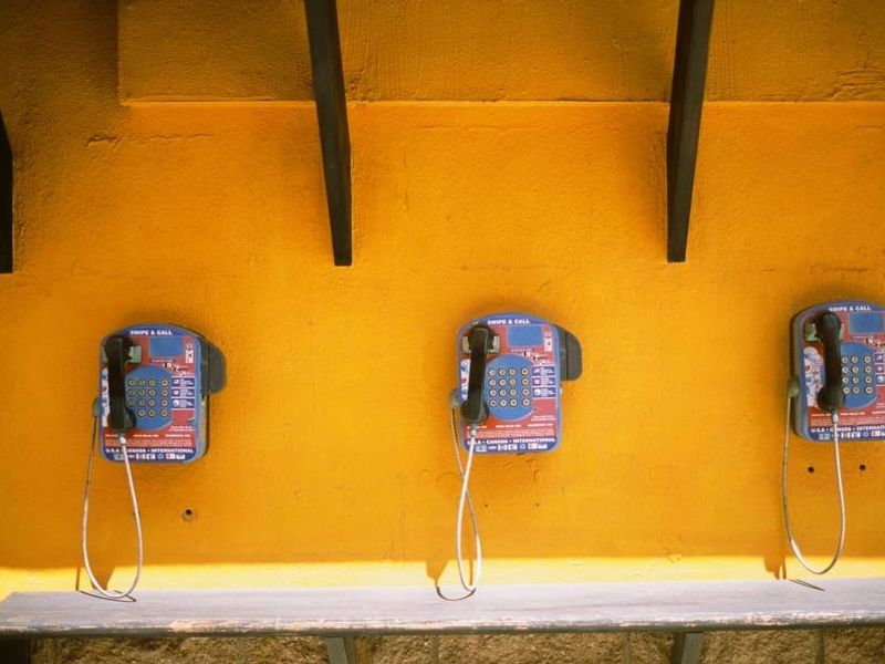 Trois téléphones publics accrochés à un mur jaune