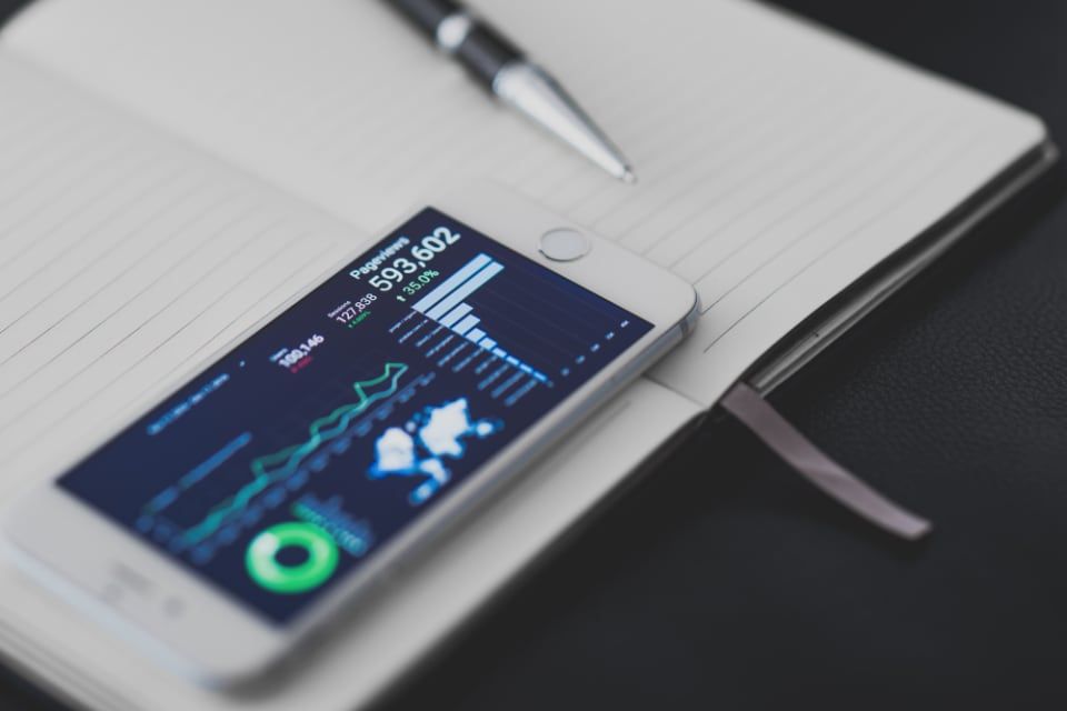 Un smartphone affichant des graphiques, posé sur un carnet