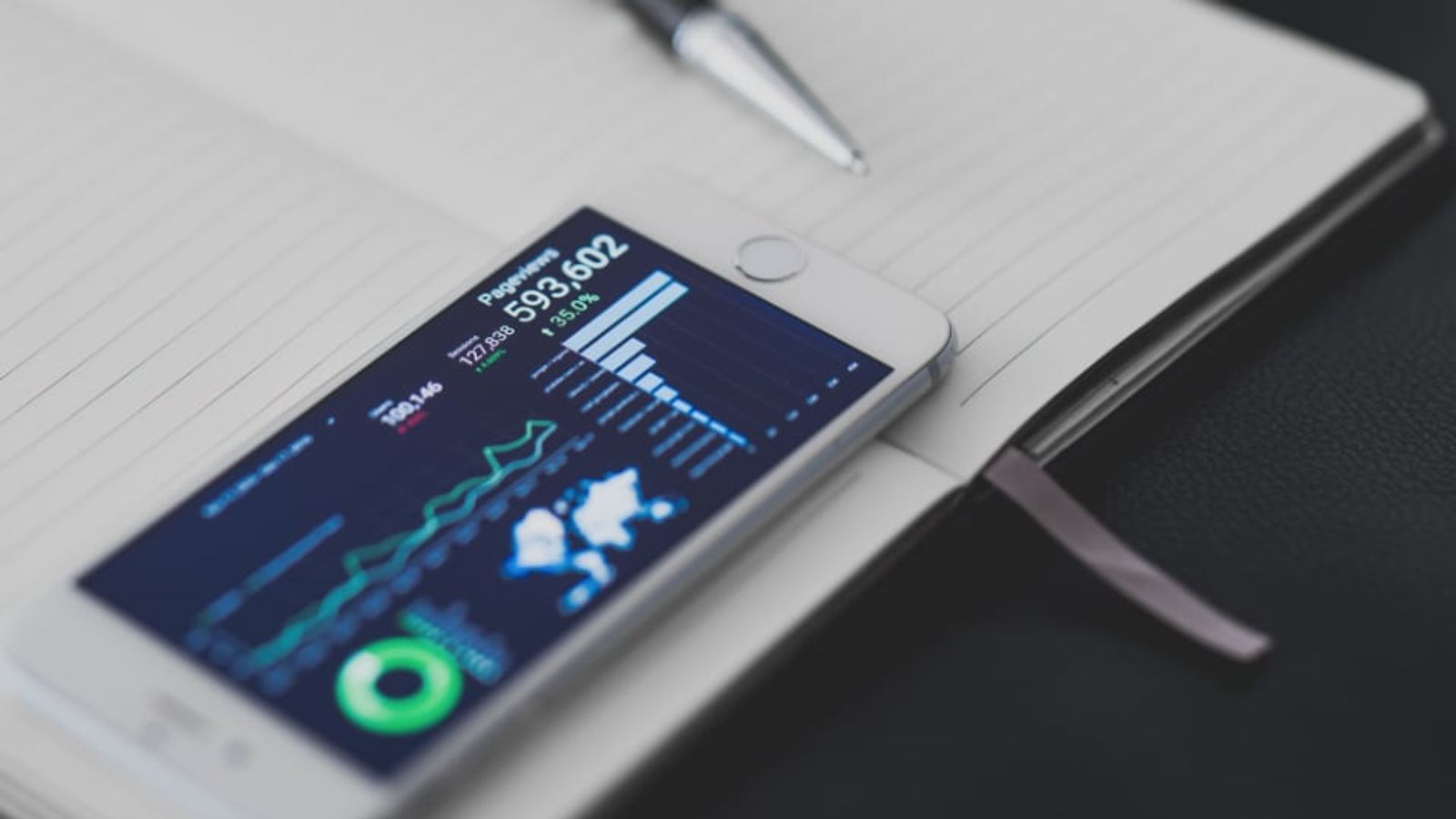 Un smartphone affichant des graphiques, posé sur un carnet
