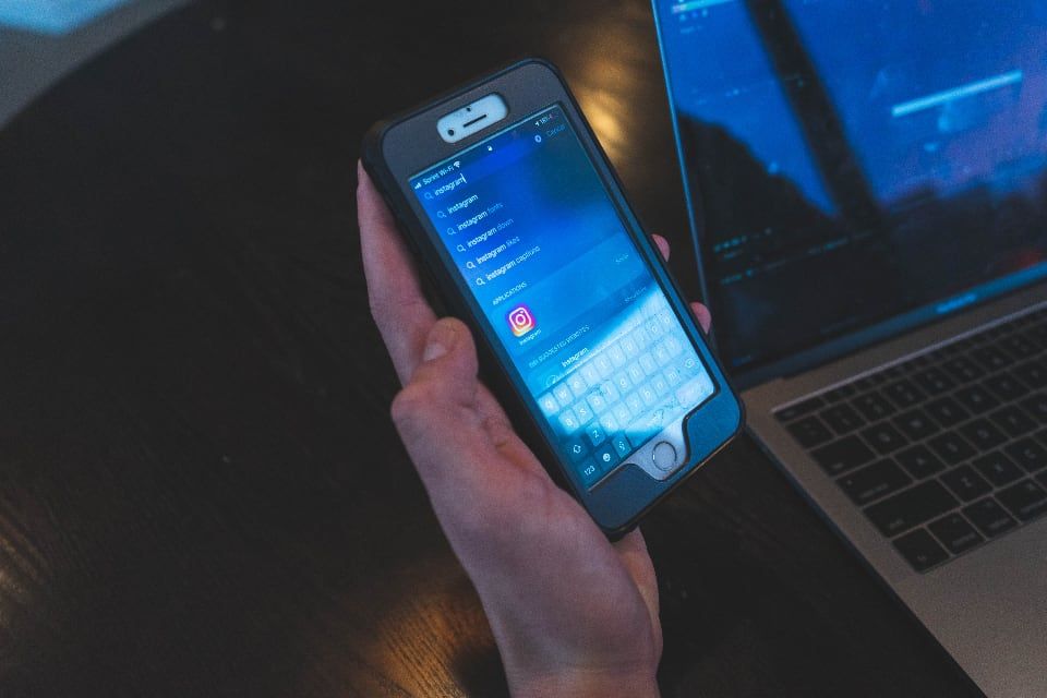 Une main tenant un smartphone devant un ordinateur portable