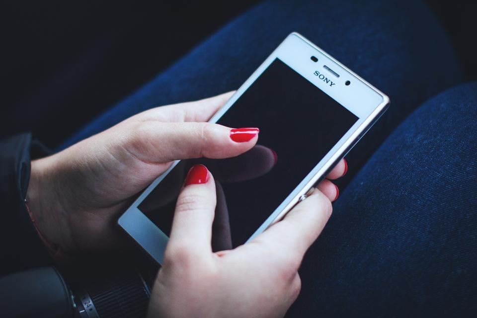 Des mains aux ongles rouges tenant un smartphone