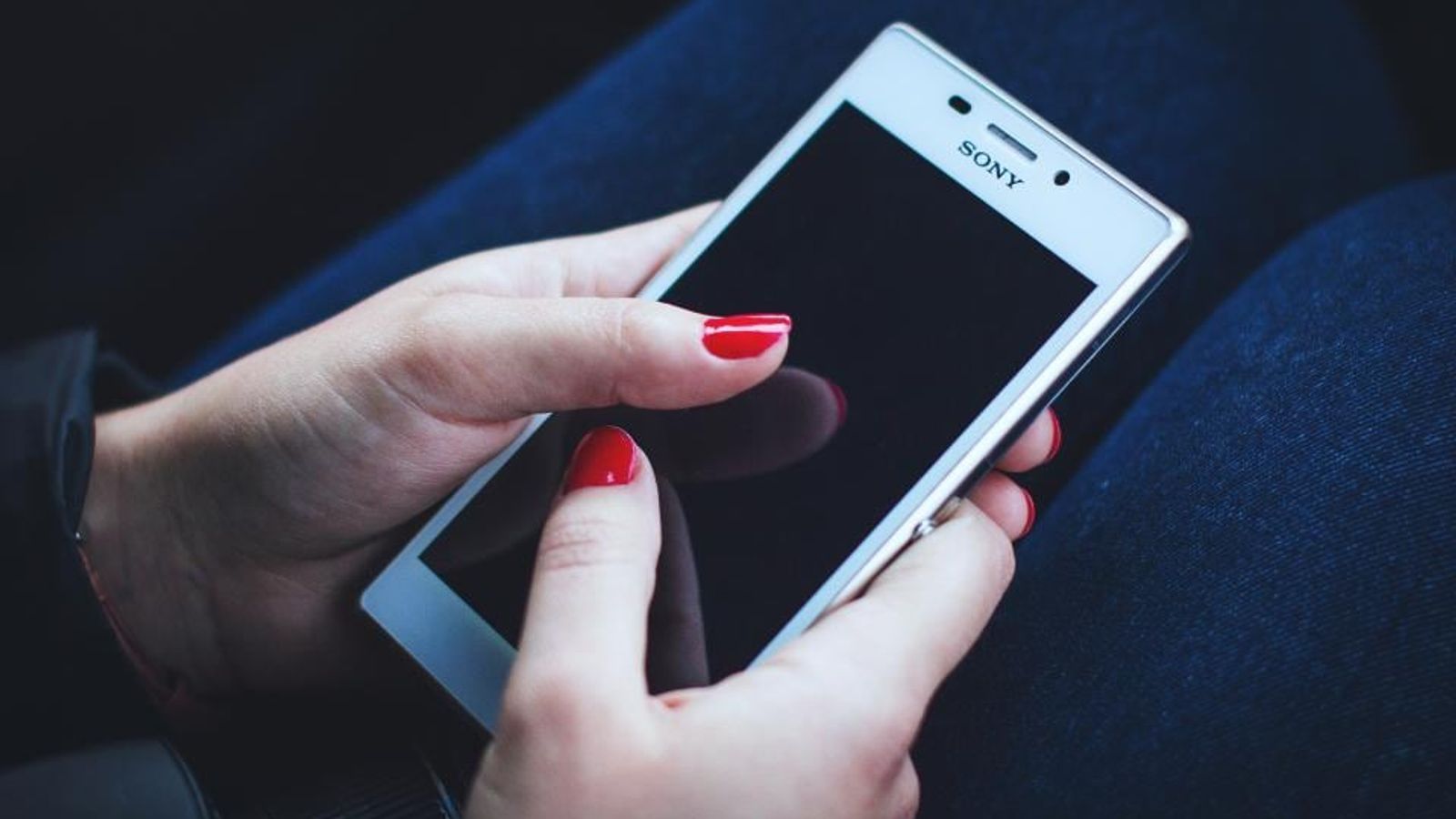 Des mains aux ongles rouges tenant un smartphone