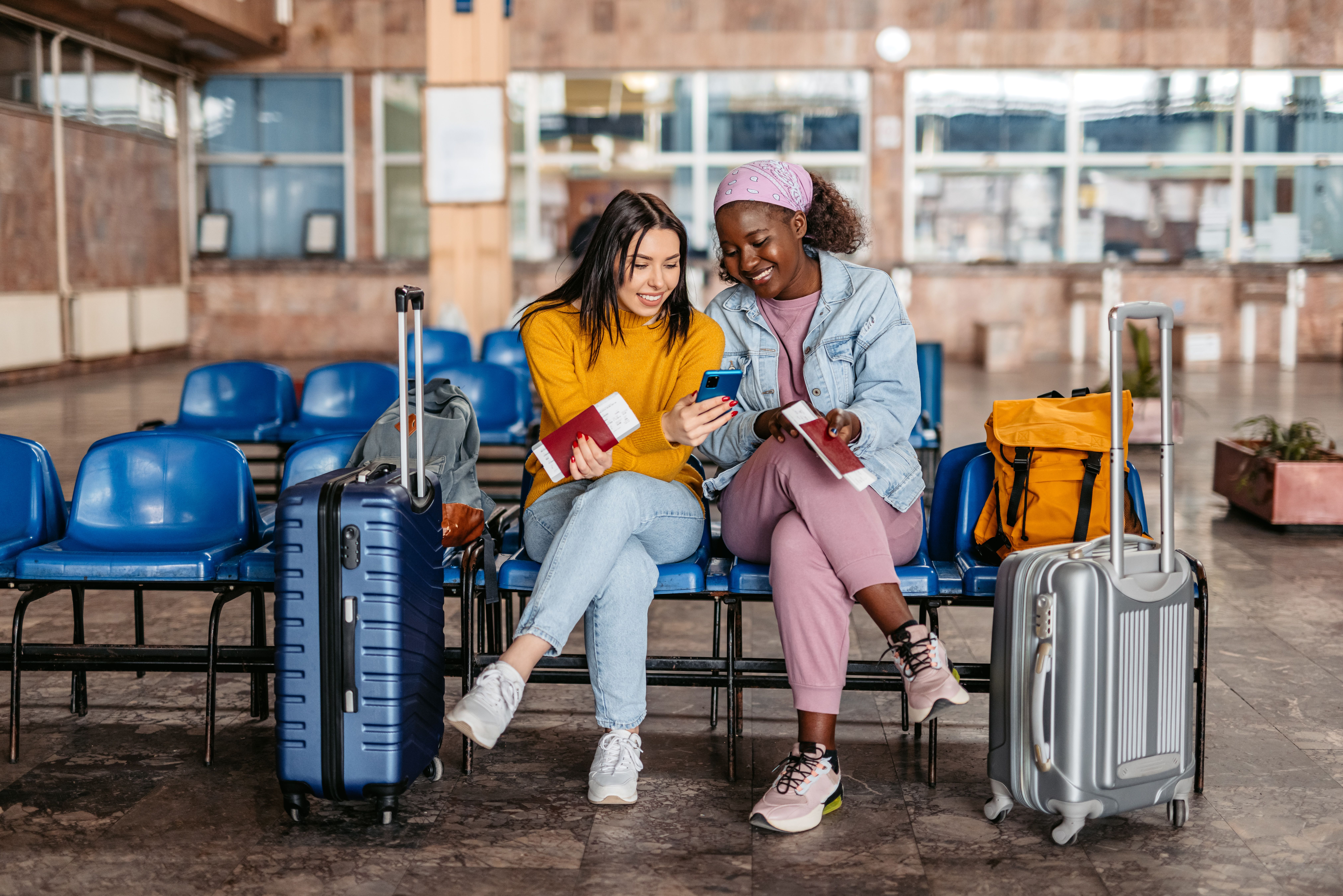 Two young female tourists looking at their phone while waiting for a train or a bus at the station.