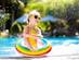 Young girl in a yellow swimsuit and yellow heart-shaped glasses with a rainbow pool ring in a swimming pool
