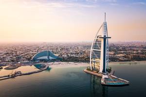 Aerial sunrise view of the sail-shaped Burj Al Arab building in Dubai looking out to the rest of the city beyond
