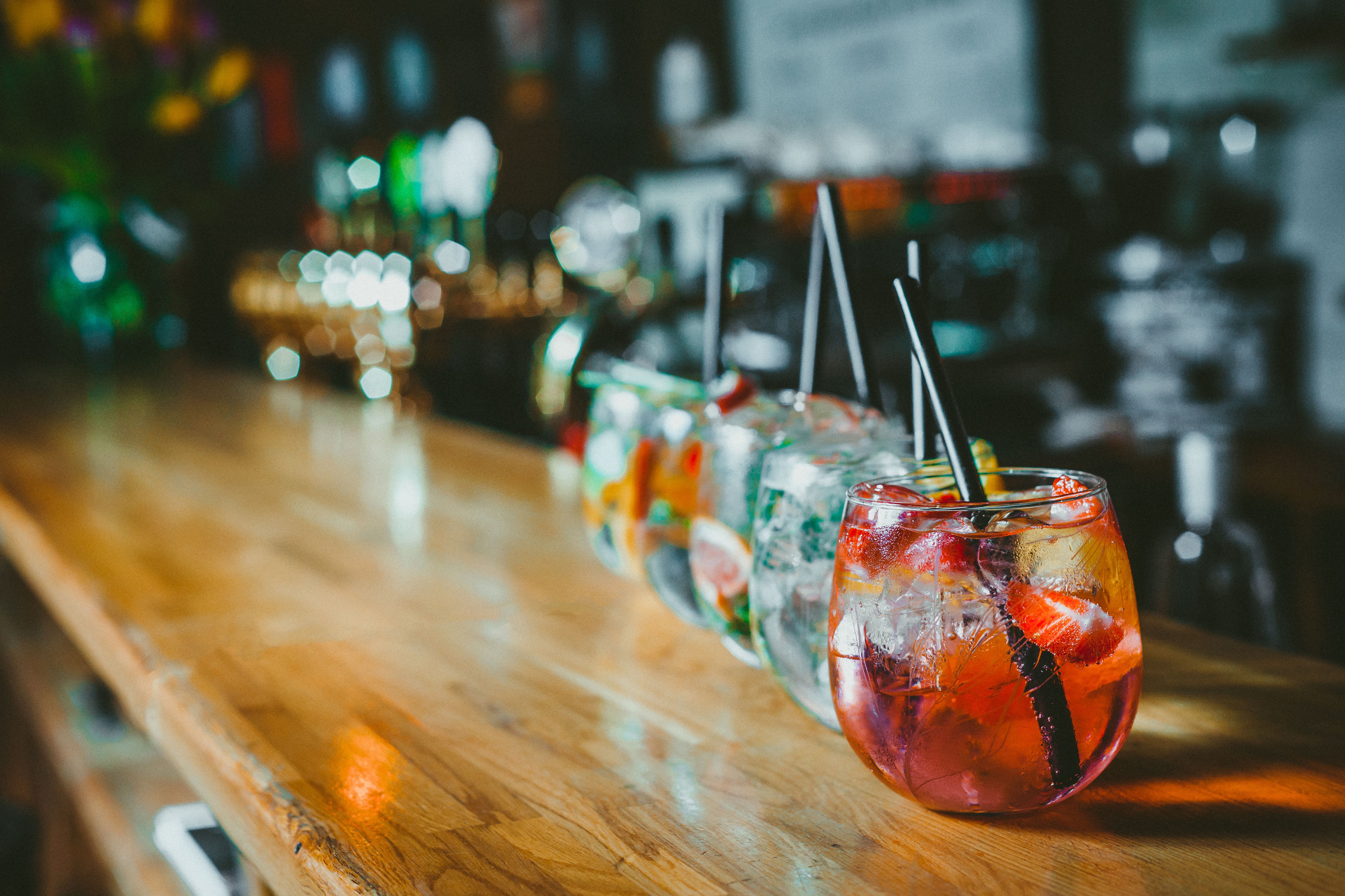 View of colourful cocktails filled with ice and fruit lined up along bar.