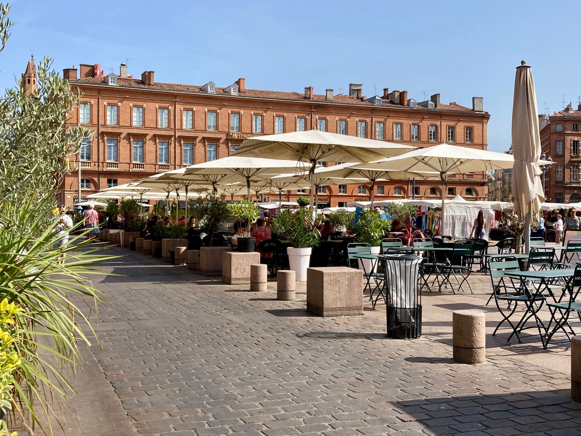 View of a café-filled plaza in front of a grand pink-brick building in Toulouse.