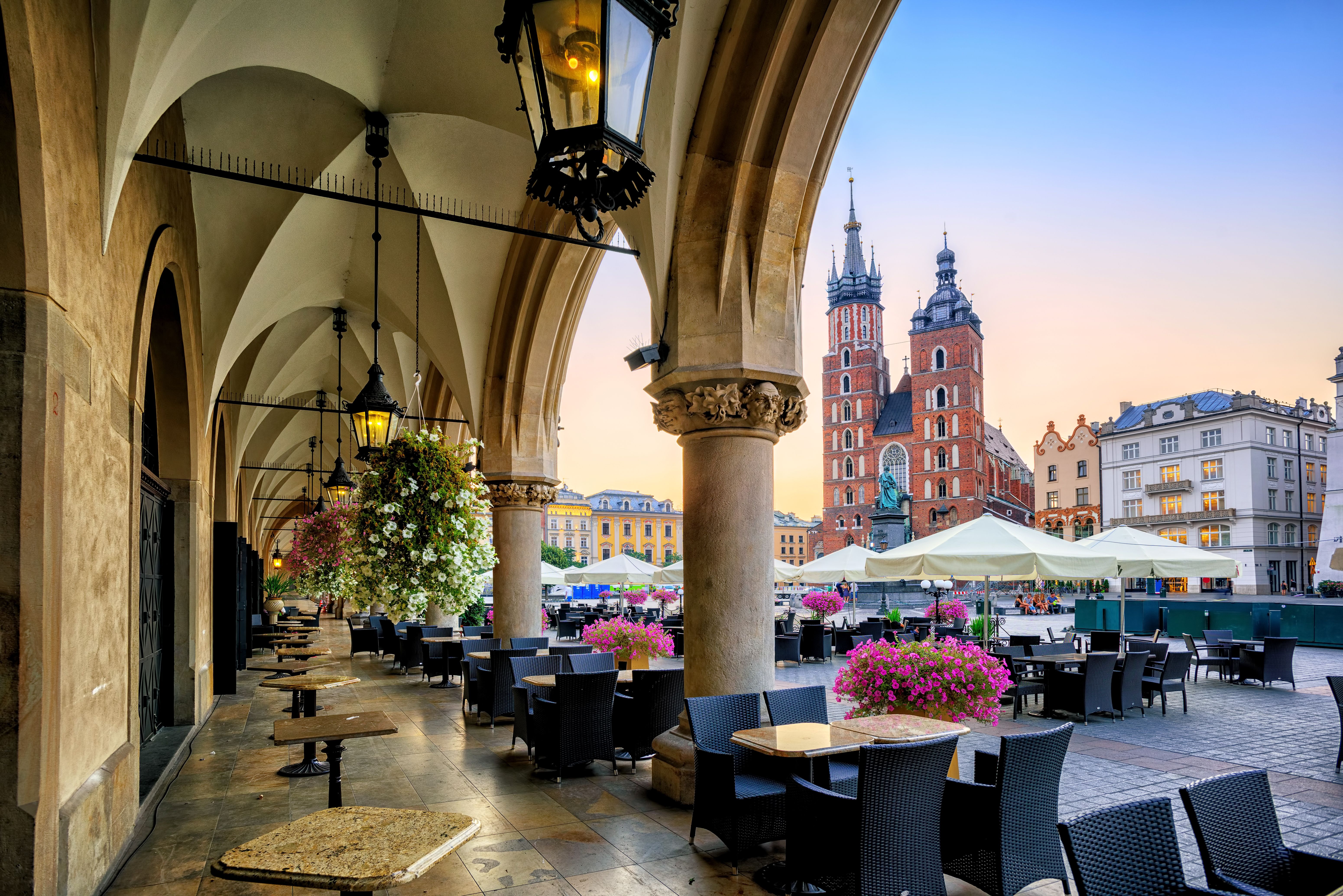 A view of the main square in Krakow old town with cafe tables and chairs and a dusky sky