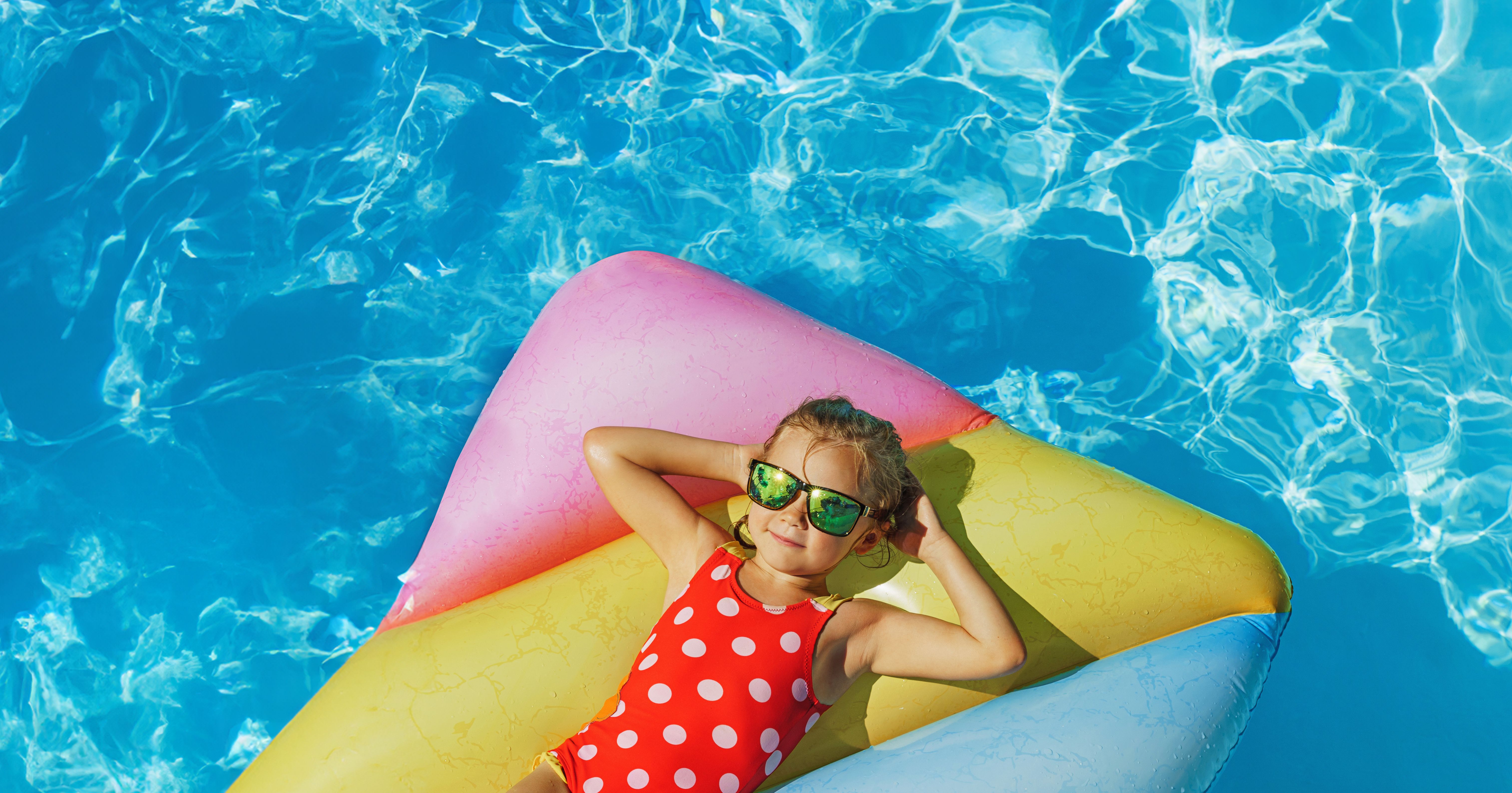 A bird's eye view of a young girl with sunglasses on floating on an inflatable in a pool