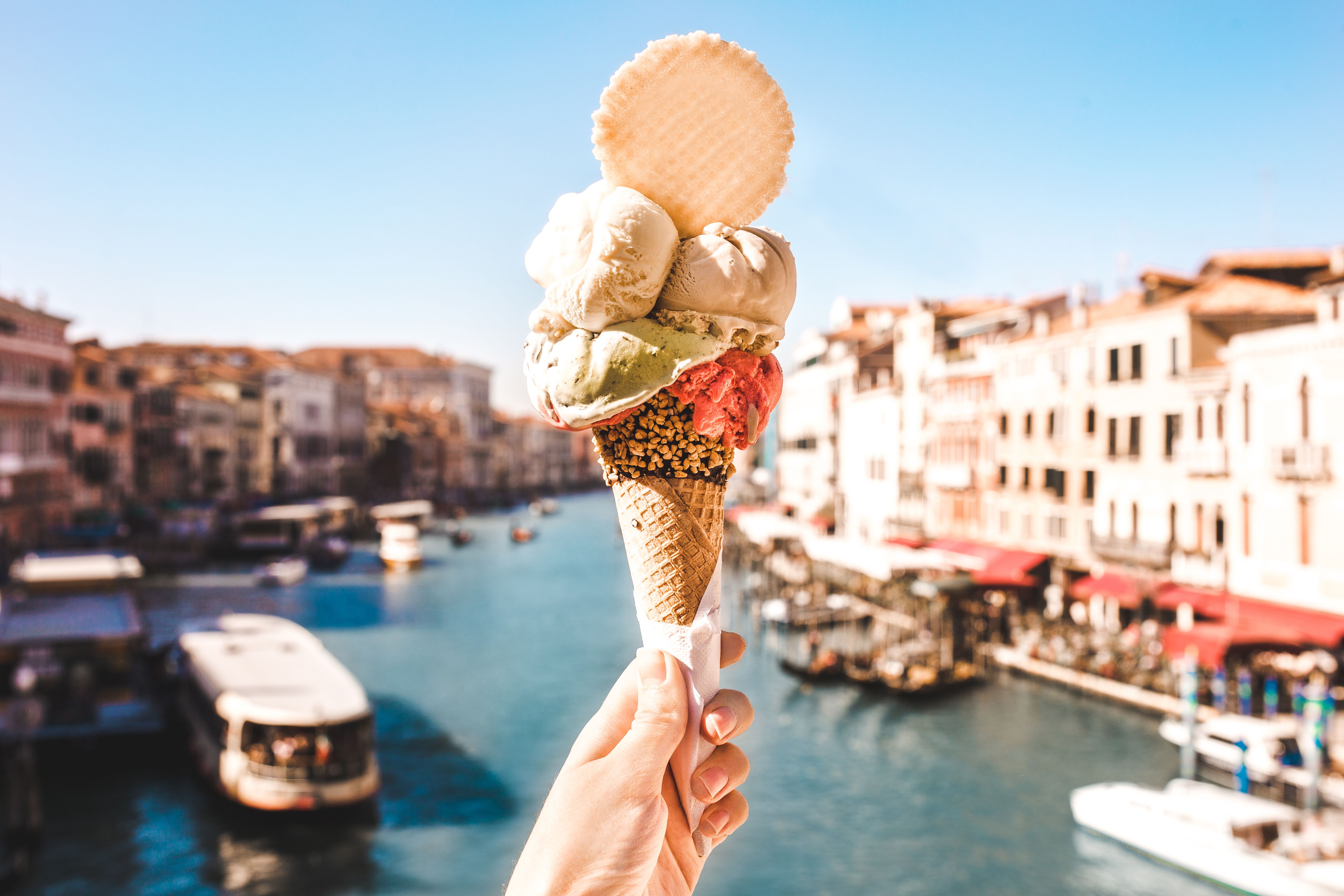 A shot of a multi-scoop ice cream cone and wafer being held in front of a river scene