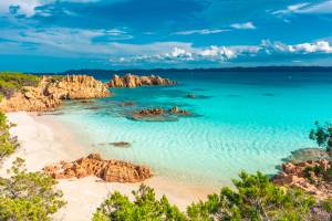 View of a beach with pinkish sands and clear, turquoise waters surrounded by golden rocks in Sardinia
