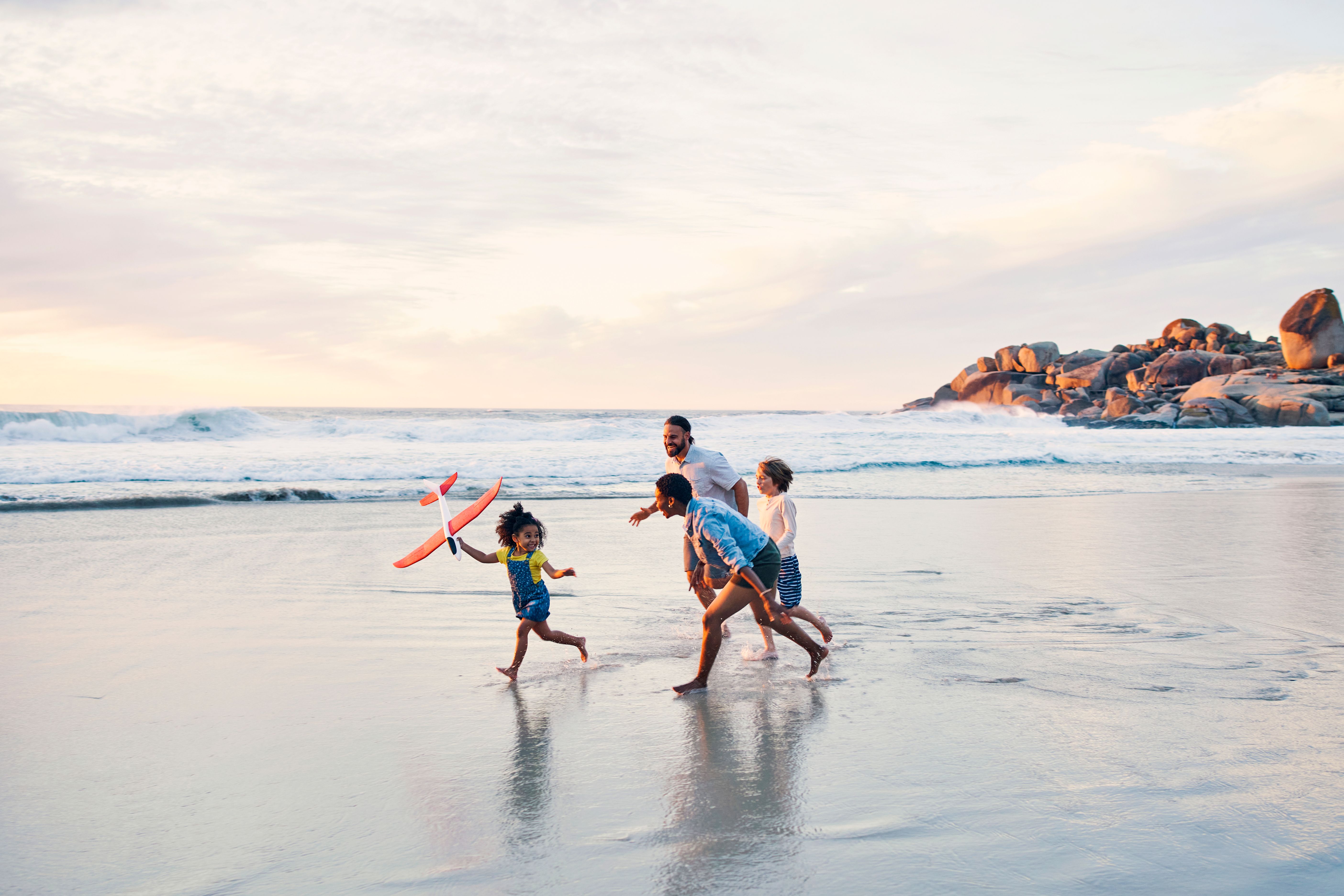 A happy family running and playing on the shore of the sea laughing and playing with with toys at sunset