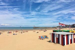 View of the golden, sandy Margate beach with sun-loungers dotted on the sand and the UK flag waving in the breeze