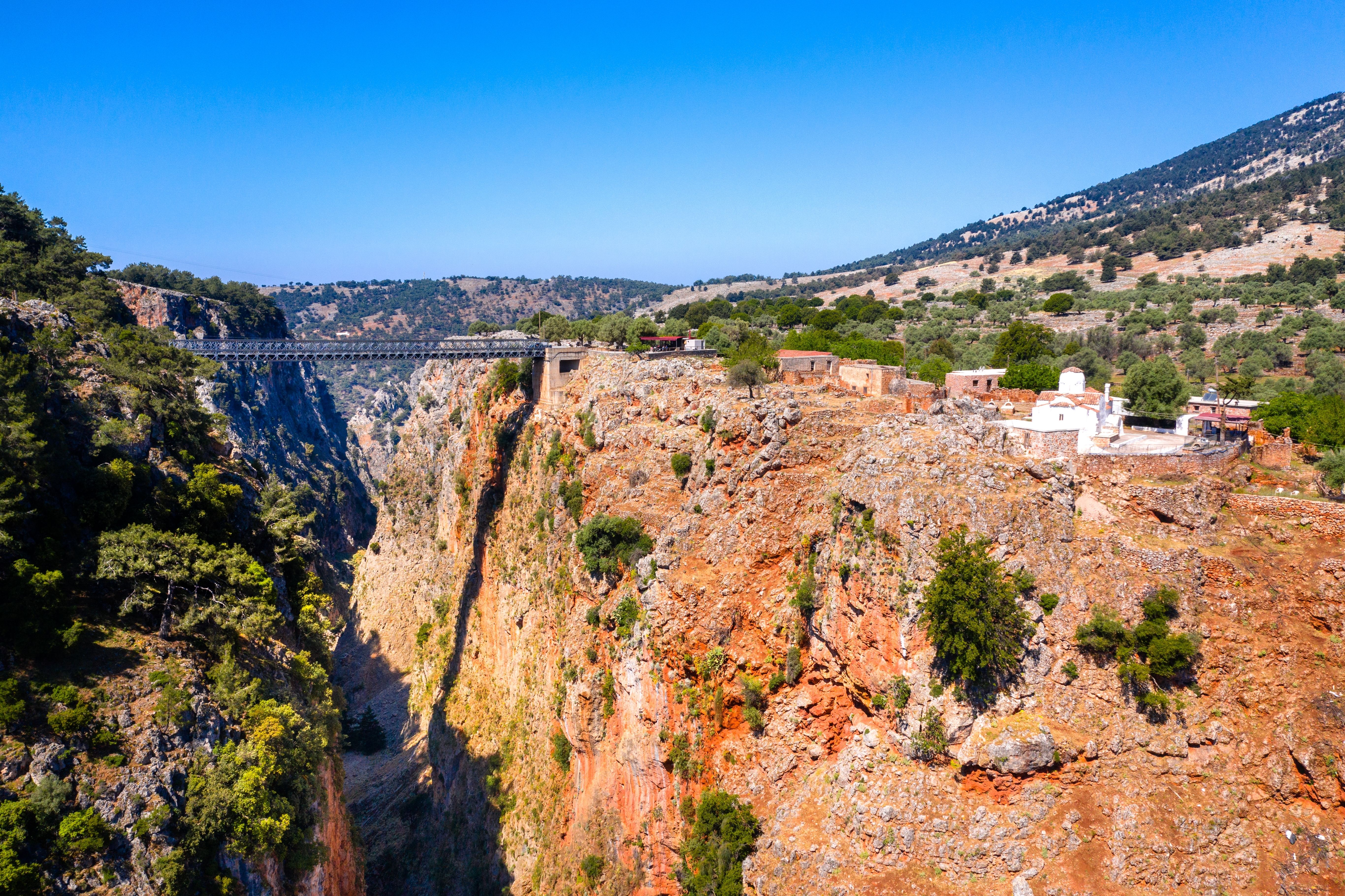 View of a barren red gorge with a metal bridge connecting the two sides.