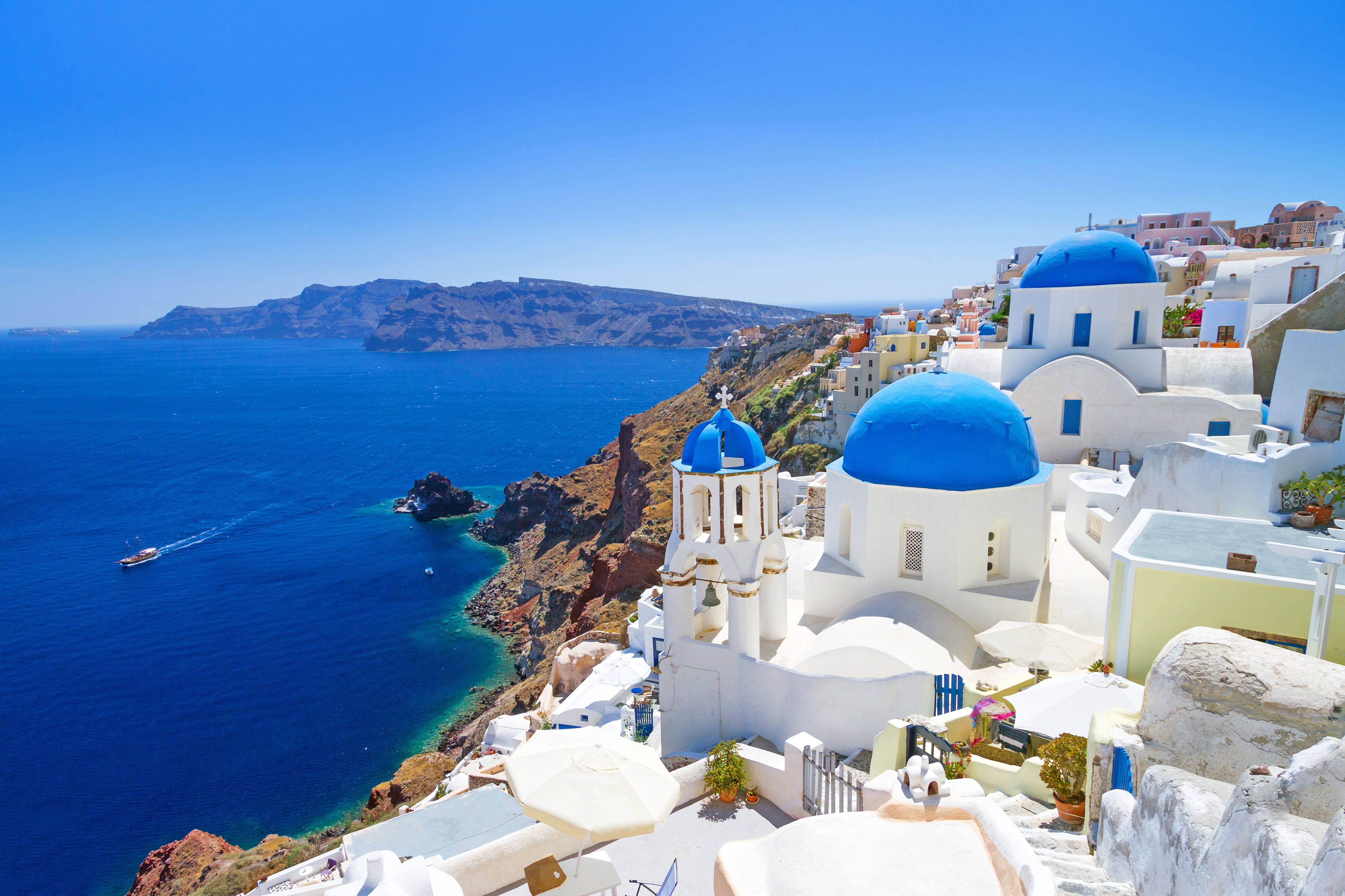 Blue domed white churches perched high on a cliff overlooking the blue Mediterranean in Santorini, Greece