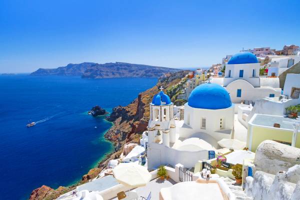Blue domed white churches perched high on a cliff overlooking the blue Mediterranean in Santorini, Greece
