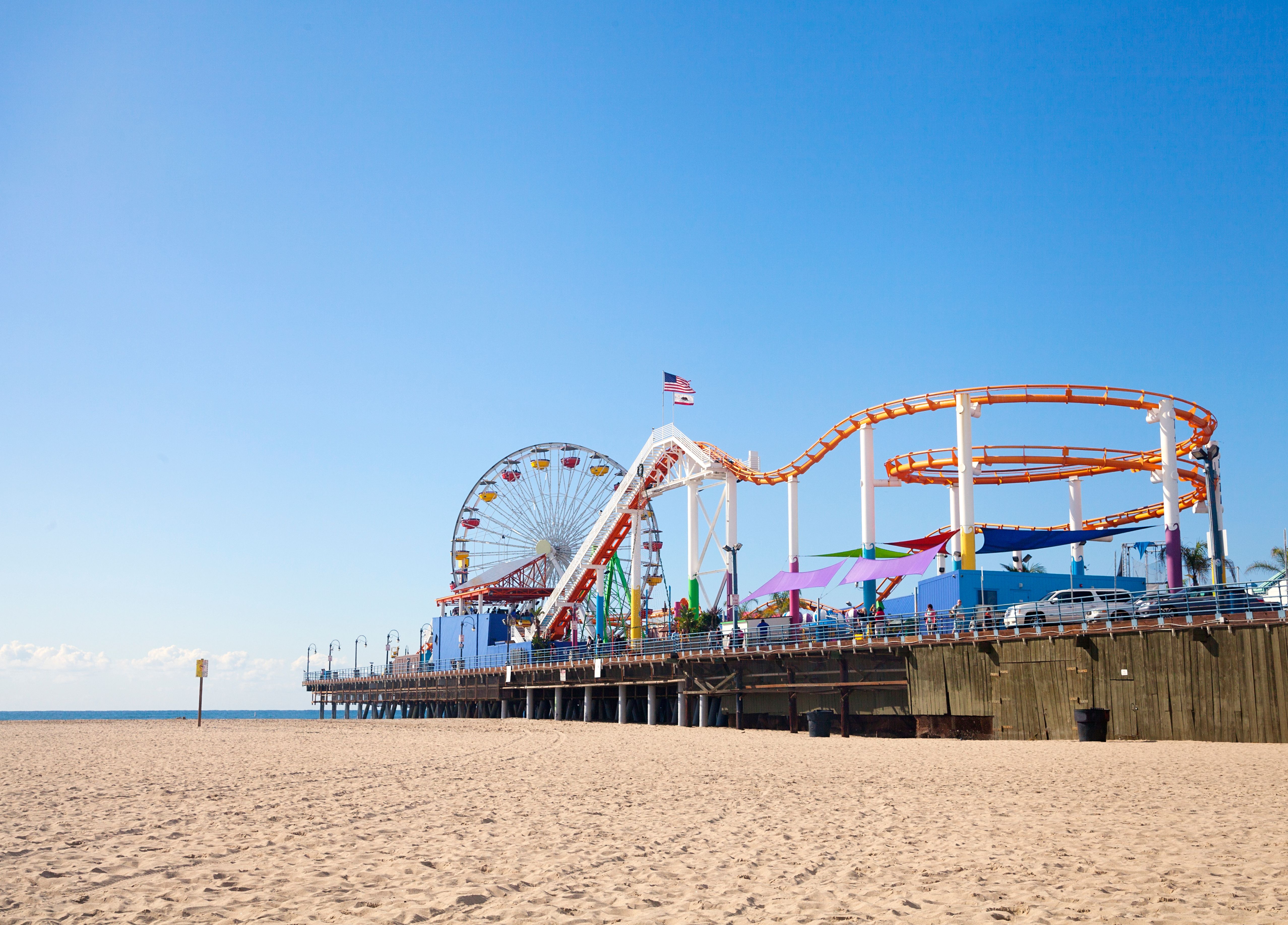 View of a fairground with a ferris wheel and small rollercoaster on the Santa Monica Beach.