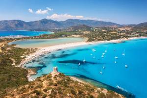 Aerial view of Porto Giunco beach in Sardinia with turquoise bays, white sand and mountains in the distance